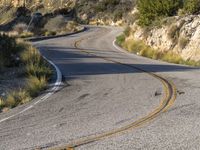 the curved road has two yellow lines on it near the mountain and the hills behind