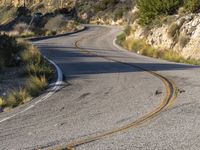 the curved road has two yellow lines on it near the mountain and the hills behind