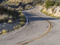 the curved road has two yellow lines on it near the mountain and the hills behind