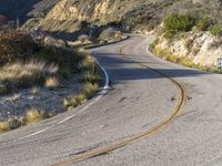 the curved road has two yellow lines on it near the mountain and the hills behind