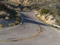 the curved road has two yellow lines on it near the mountain and the hills behind