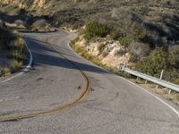 the curved road has two yellow lines on it near the mountain and the hills behind