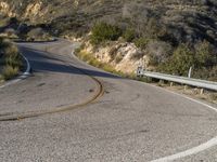 the curved road has two yellow lines on it near the mountain and the hills behind