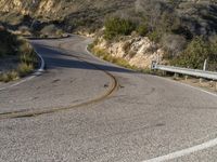 the curved road has two yellow lines on it near the mountain and the hills behind