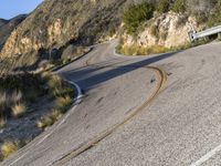 the curved road has two yellow lines on it near the mountain and the hills behind