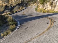 the curved road has two yellow lines on it near the mountain and the hills behind