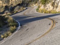 the curved road has two yellow lines on it near the mountain and the hills behind