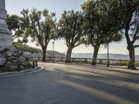 a city road going down the hill with trees on both sides of it and a stone block in the middle of the street