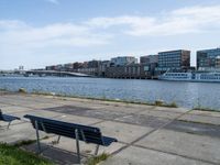 a city view with boats near some water and two park benches sitting on a cement path