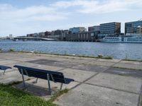 a city view with boats near some water and two park benches sitting on a cement path