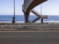 a long bridge spanning over the ocean and under it is palm trees and a bench