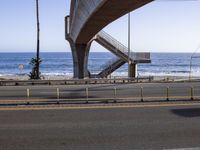 a long bridge spanning over the ocean and under it is palm trees and a bench