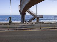 a long bridge spanning over the ocean and under it is palm trees and a bench