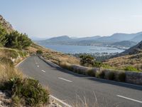 a curved highway winds through a scenic mountainous area to the ocean and mountains nearby, overlooking a bay, and distant mountains