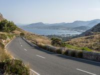 a curved highway winds through a scenic mountainous area to the ocean and mountains nearby, overlooking a bay, and distant mountains