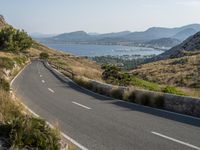 a curved highway winds through a scenic mountainous area to the ocean and mountains nearby, overlooking a bay, and distant mountains