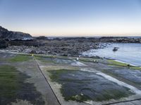 a long path between large rocks leading to the sea next to a body of water