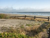 a beach with an empty road by the water and grass by the shore line and a bench is in front of the sand