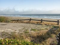 a beach with an empty road by the water and grass by the shore line and a bench is in front of the sand