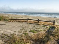 a beach with an empty road by the water and grass by the shore line and a bench is in front of the sand