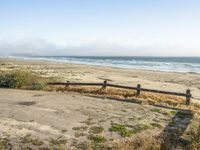 a beach with an empty road by the water and grass by the shore line and a bench is in front of the sand