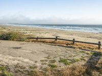 a beach with an empty road by the water and grass by the shore line and a bench is in front of the sand