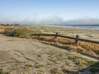 a beach with an empty road by the water and grass by the shore line and a bench is in front of the sand