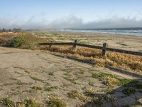 a beach with an empty road by the water and grass by the shore line and a bench is in front of the sand