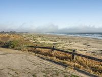 a beach with an empty road by the water and grass by the shore line and a bench is in front of the sand