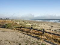 a beach with an empty road by the water and grass by the shore line and a bench is in front of the sand