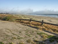 a beach with an empty road by the water and grass by the shore line and a bench is in front of the sand