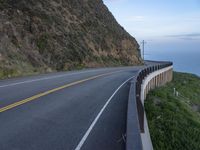 a view of a long winding road on the side of the ocean with a blue sky and clouds