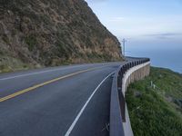 a view of a long winding road on the side of the ocean with a blue sky and clouds