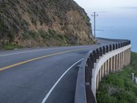 a view of a long winding road on the side of the ocean with a blue sky and clouds