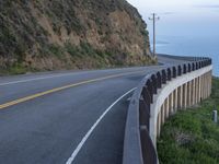 a view of a long winding road on the side of the ocean with a blue sky and clouds