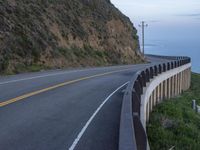 a view of a long winding road on the side of the ocean with a blue sky and clouds