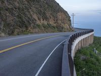 a view of a long winding road on the side of the ocean with a blue sky and clouds