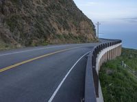 a view of a long winding road on the side of the ocean with a blue sky and clouds