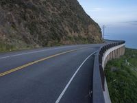 a view of a long winding road on the side of the ocean with a blue sky and clouds