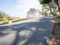 a person riding down a hill with trees on both sides of the road and hills covered in green vegetation