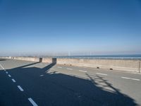 a bridge over the ocean with construction equipment in the background and two people walking on it