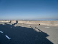 a bridge over the ocean with construction equipment in the background and two people walking on it