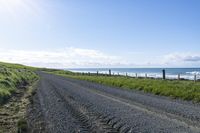 a gravel road that is surrounded by grass and water and the beach is in the background