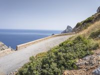 two motorcycles traveling on a narrow paved road by the ocean with mountains in the background