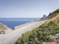 two motorcycles traveling on a narrow paved road by the ocean with mountains in the background