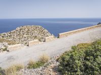 two motorcycles traveling on a narrow paved road by the ocean with mountains in the background