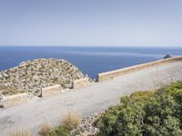 two motorcycles traveling on a narrow paved road by the ocean with mountains in the background