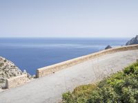 two motorcycles traveling on a narrow paved road by the ocean with mountains in the background