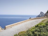 two motorcycles traveling on a narrow paved road by the ocean with mountains in the background