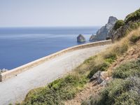 two motorcycles traveling on a narrow paved road by the ocean with mountains in the background